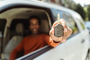 Selective focus, closeup, African American man sitting in car behind wheel showing car key